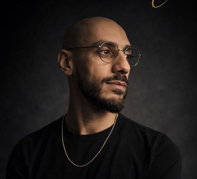 Man wearing glasses and a black shirt against a dark background